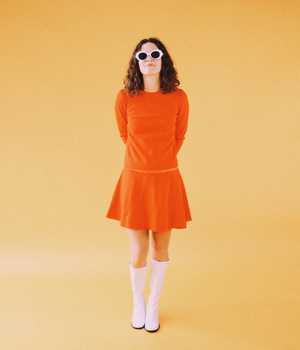 Modell i tettsittende, oransjefargede kjole med kort ben